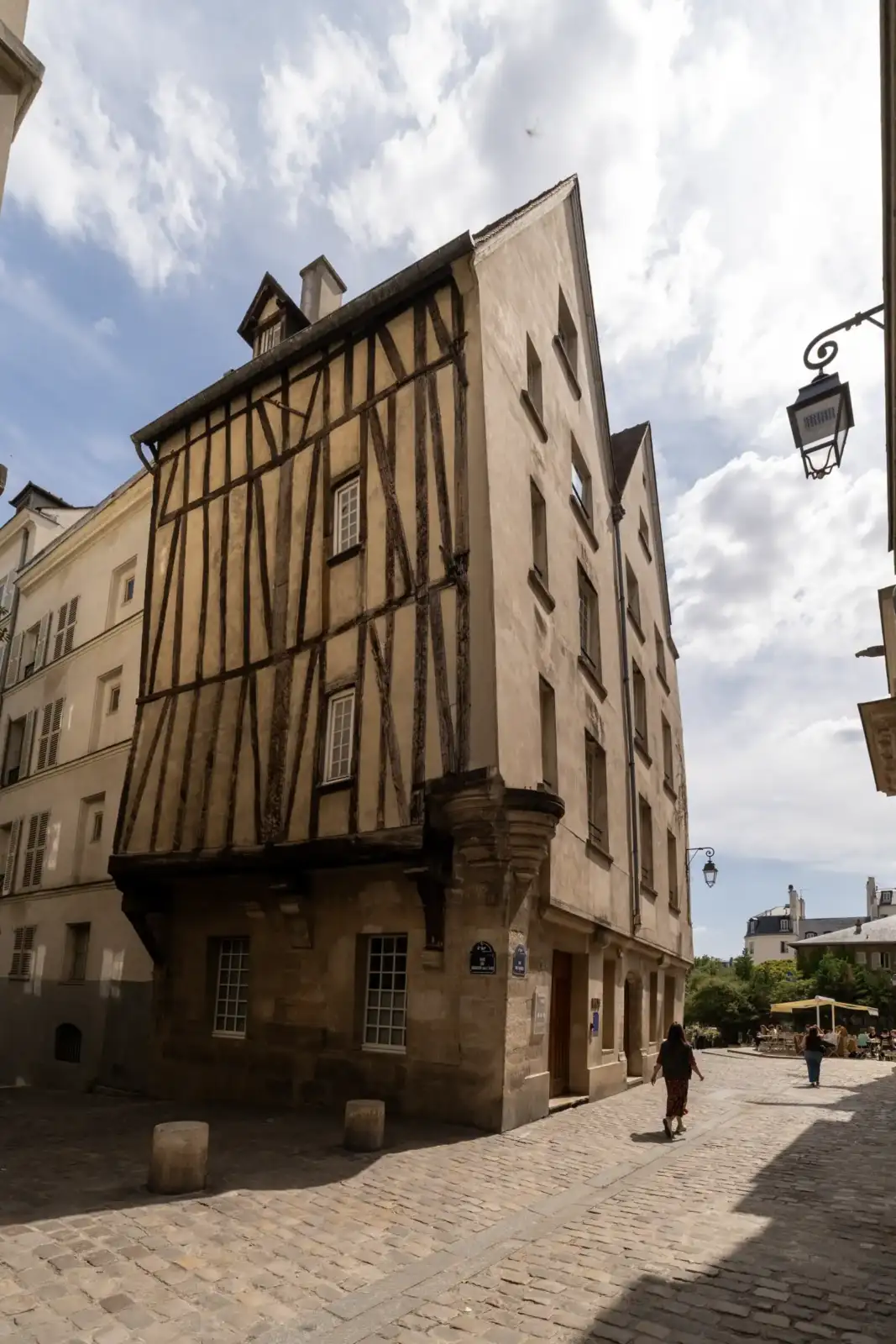 Une charmante maison à colombages ancienne domine une rue pavée sous un ciel nuageux à Paris.