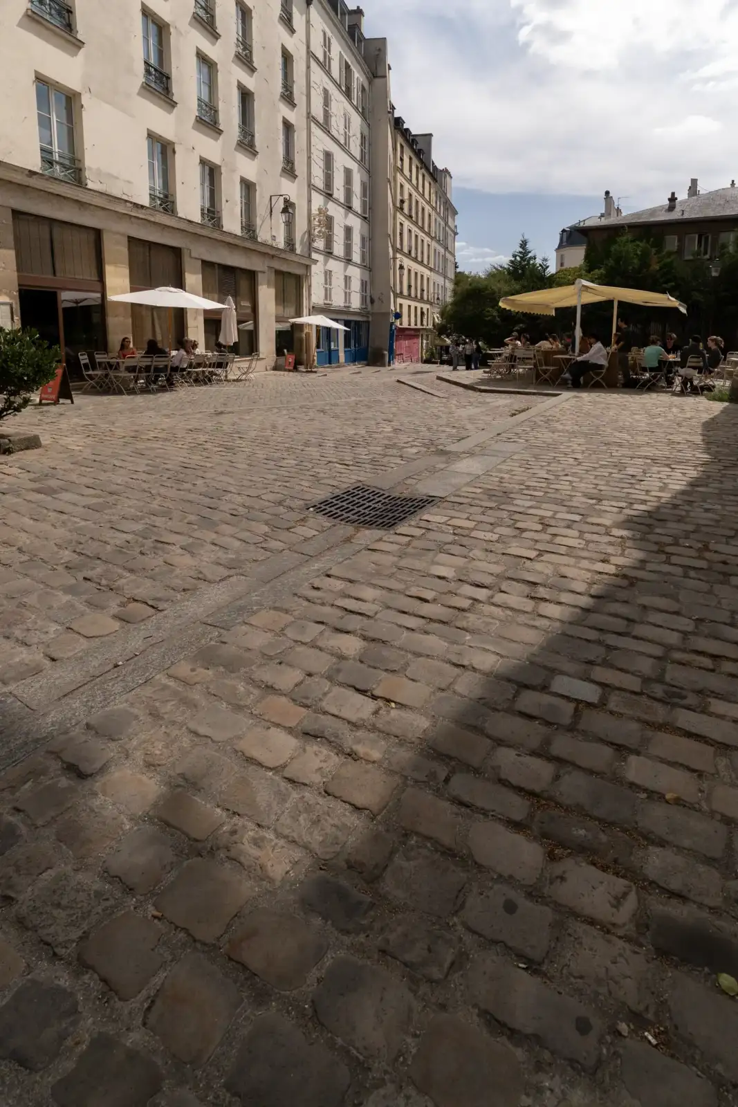 Une charmante place pavée à Paris entourée d'immeubles historiques et de terrasses animées.