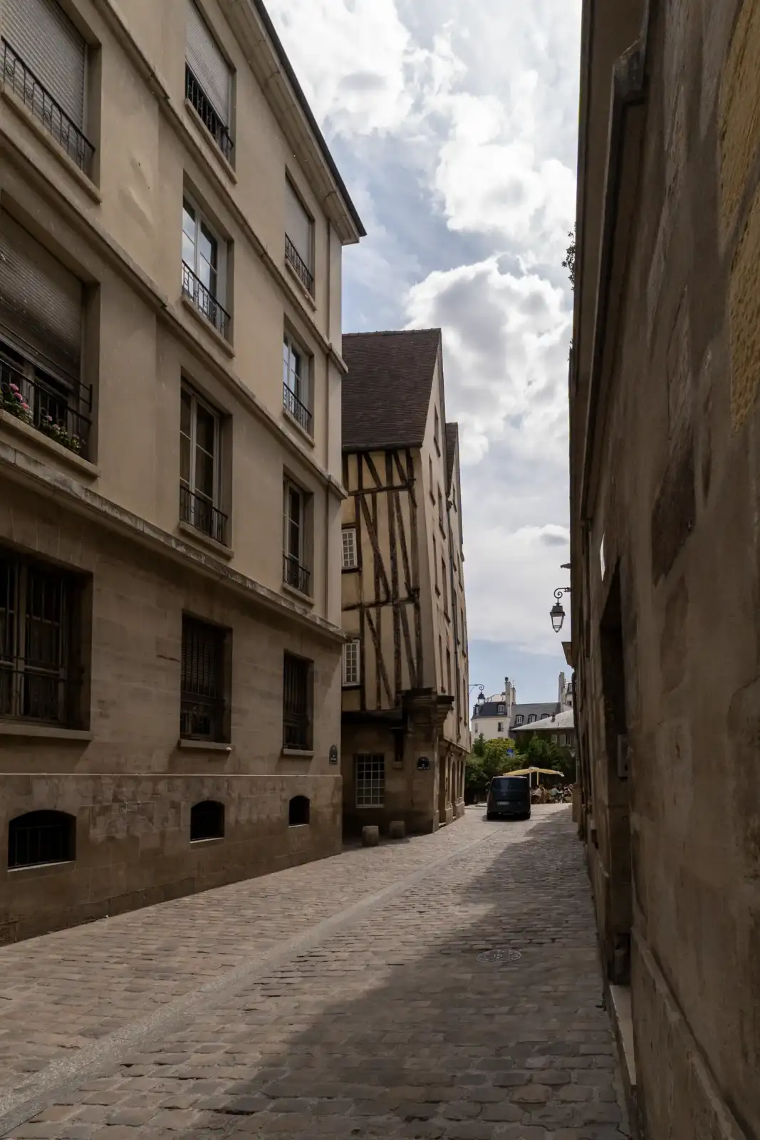 Une ruelle pavée étroite bordée d'immeubles anciens sous un ciel nuageux à Paris.