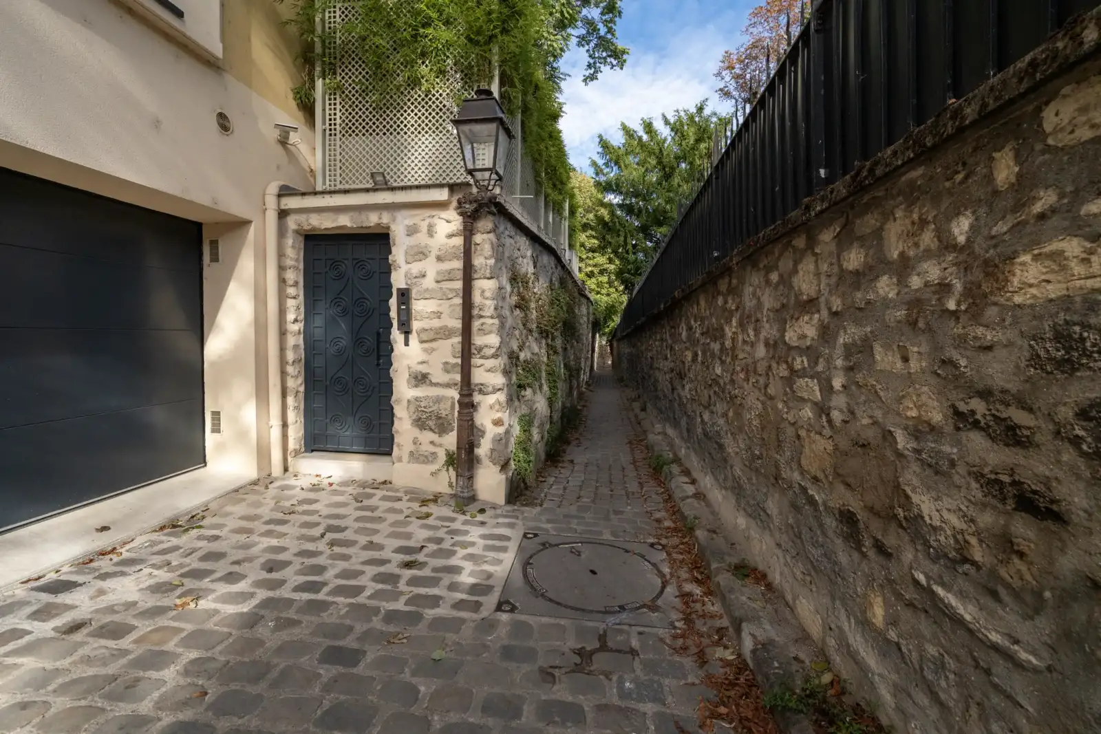 Une ruelle pavée étroite à Paris, bordée d'un mur de pierre et d'un lampadaire.