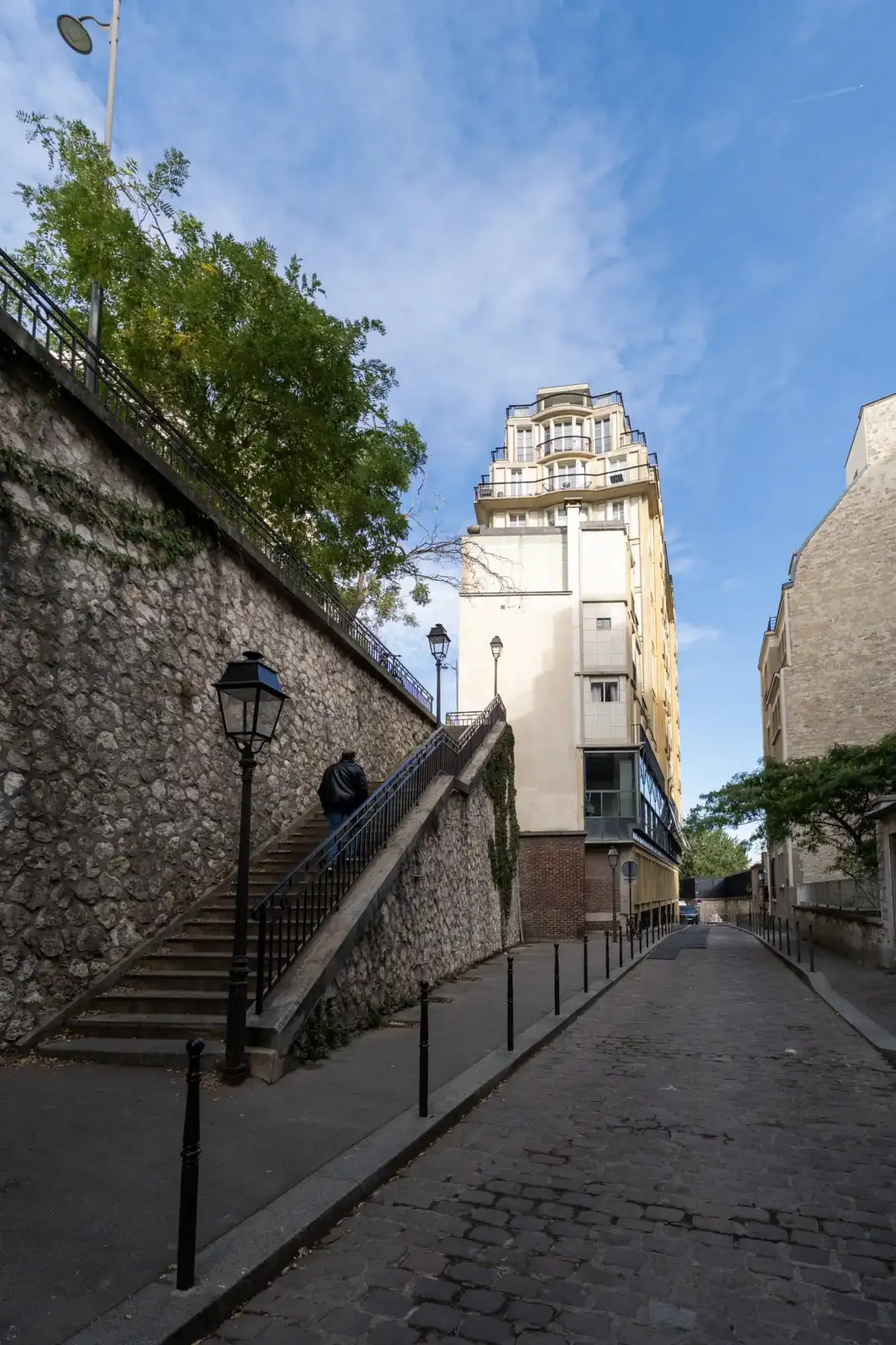 Un piéton monte un escalier en pierre bordé d'un mur ancien à Paris.
