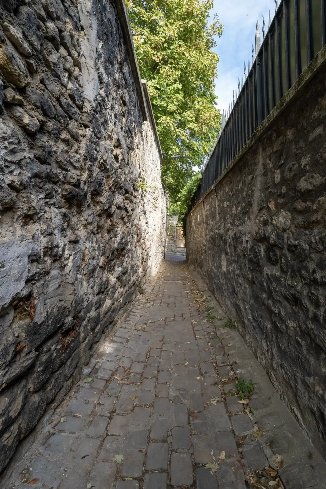 Une ruelle pavée étroite bordée de hauts murs en pierre à Paris.