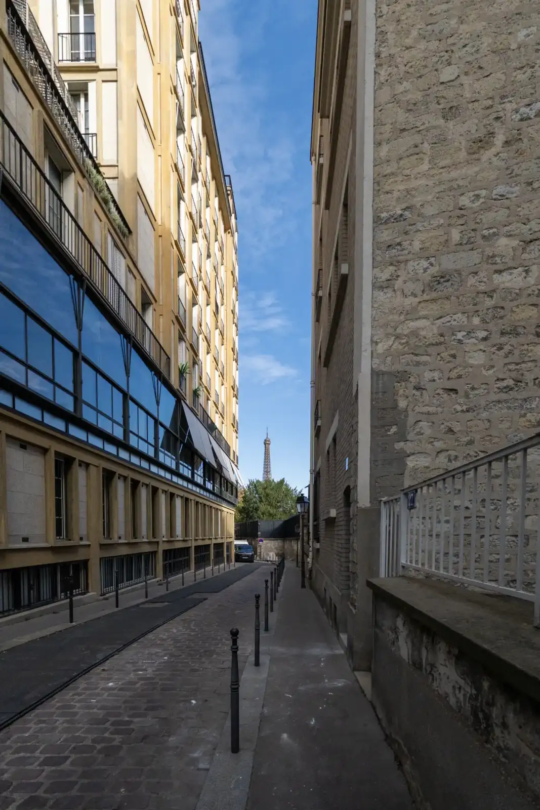 Une ruelle étroite et pavée à Paris encadrée par des immeubles anciens avec la tour Eiffel visible au loin