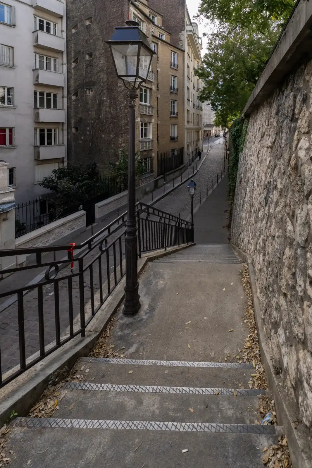 Escalier en pente bordé de murs en pierre et d'immeubles parisiens anciens.