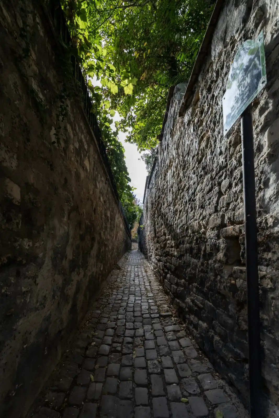 Une rue pavée étroite bordée de hauts murs en pierre avec une signalétique.