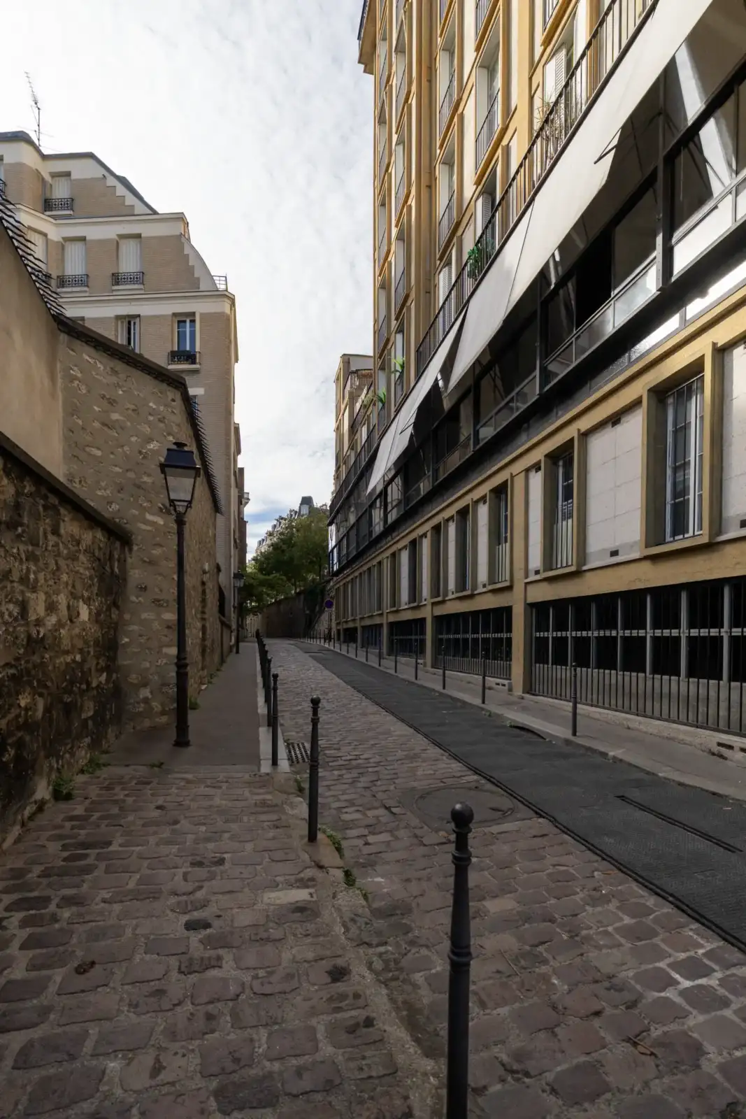 Une vue en contre-plongée montre la rue Berton pavée, encadrée de murs anciens.