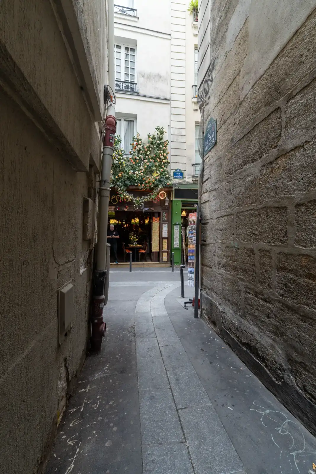Une ruelle étroite et pavée à Paris mène vers un immeuble fleuri et lumineux.