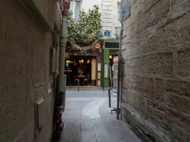 Une ruelle étroite et pavée à Paris mène vers un immeuble fleuri et lumineux.