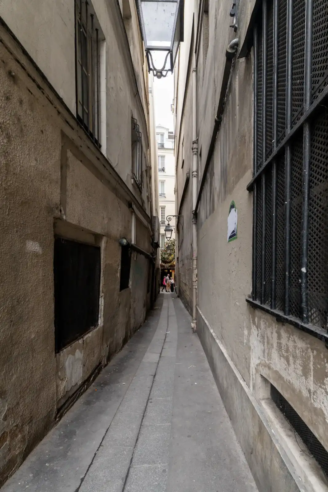 Une perspective en contre-plongée de la ruelle parisienne très étroite, entre hauts murs patinés.