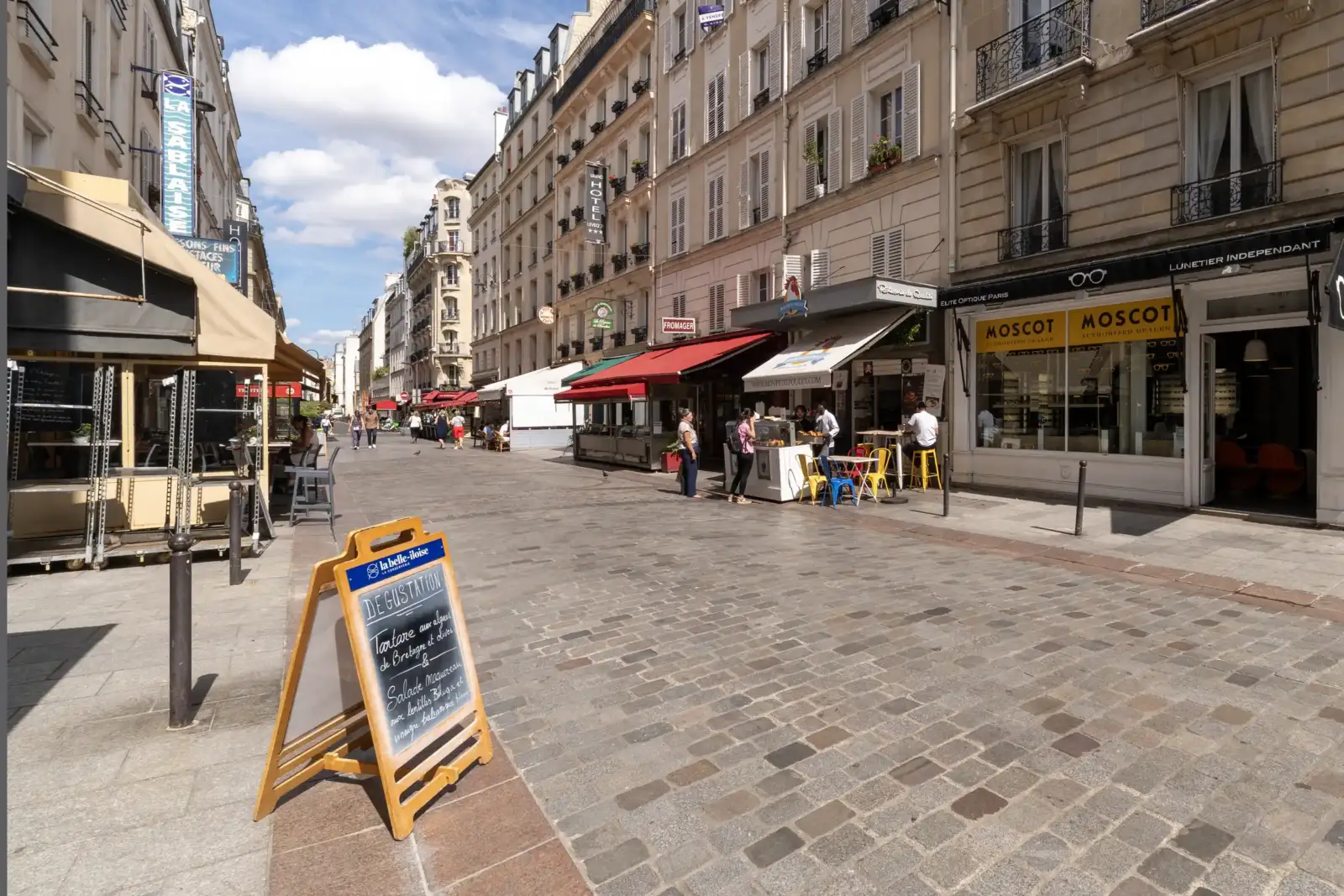 Une rue piétonne animée de Paris bordée de commerces et de façades parisiennes classiques.