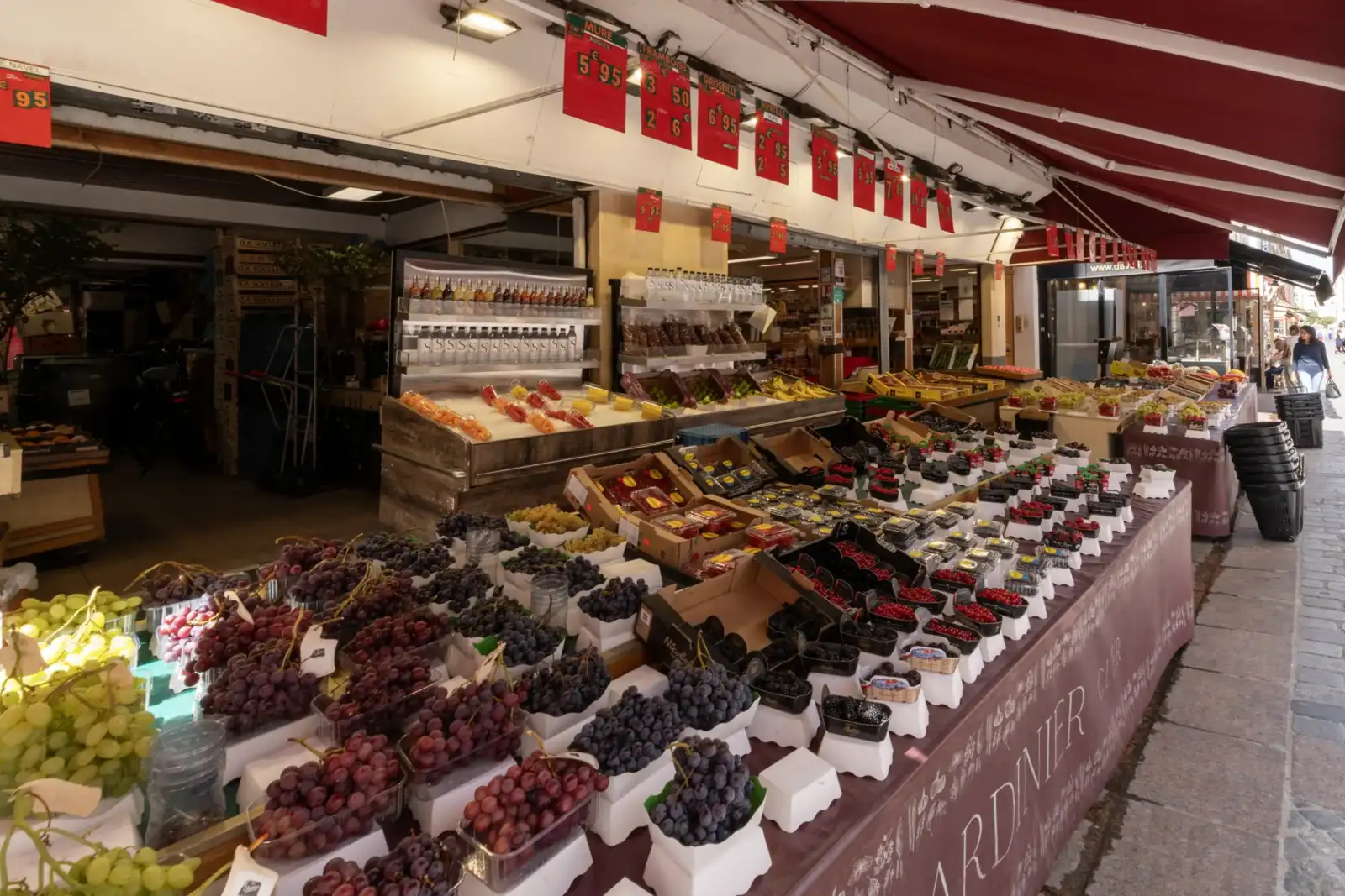 Une façade de marché parisien en plein air présente des étals remplis de raisins colorés.