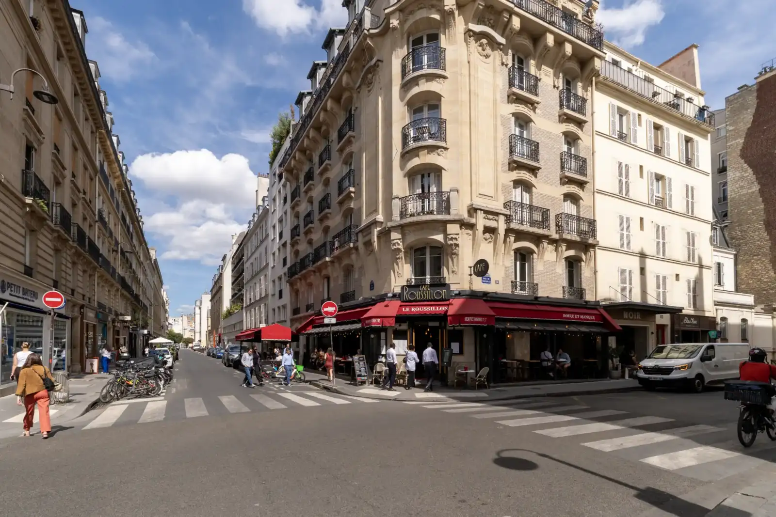 Façade élégante d'un café parisien avec des stores rouges sur une rue animée.