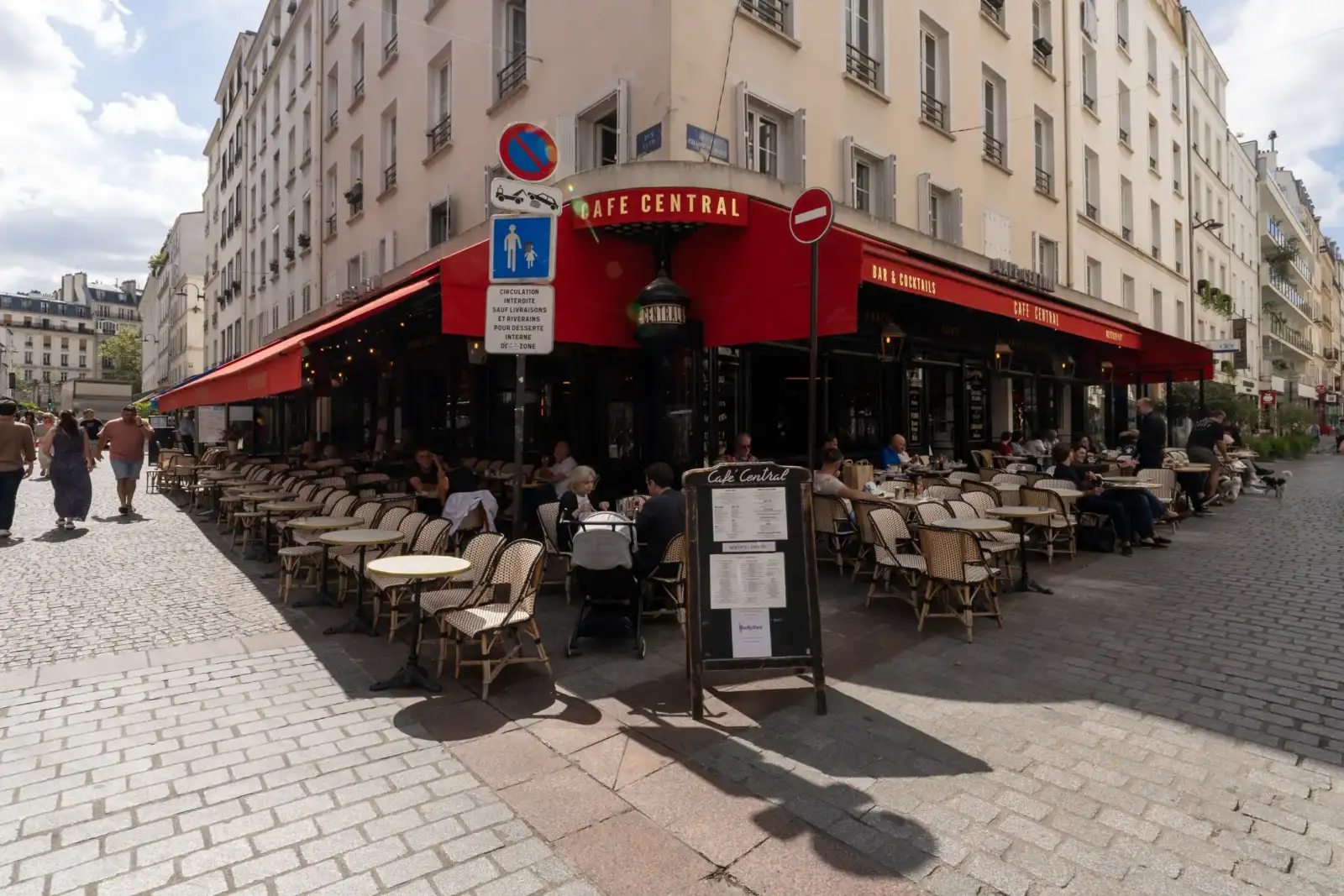 Façade animée du Café Central à Paris avec des tables en terrasse et des passants.