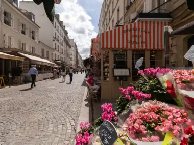 Rue piétonne pavée animée à Paris, bordée de commerces et de clients attablés.