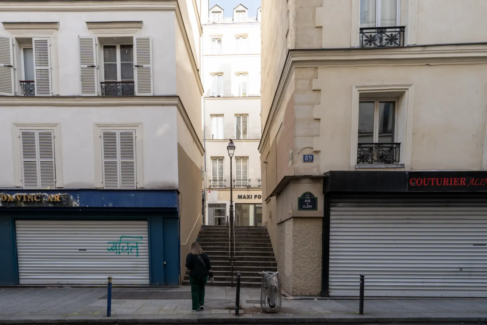 Une femme marche vers un escalier étroit entre deux immeubles parisiens du deuxième arrondissement.