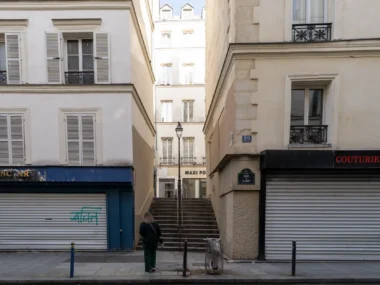 Une femme marche vers un escalier étroit entre deux immeubles parisiens du deuxième arrondissement.