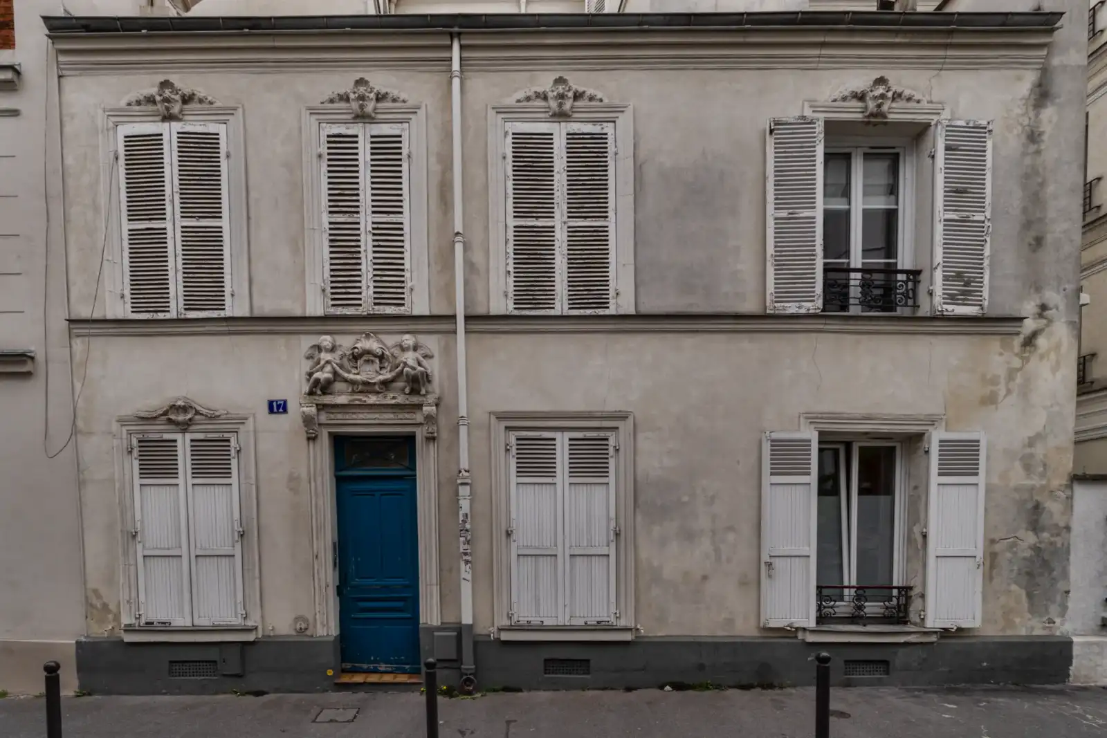 Une façade parisienne ancienne en pierre claire présente une porte bleue et des volets blancs.