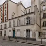 Une ruelle pavée de Paris bordée par de vieux immeubles anciens aux fenêtres persiennes.