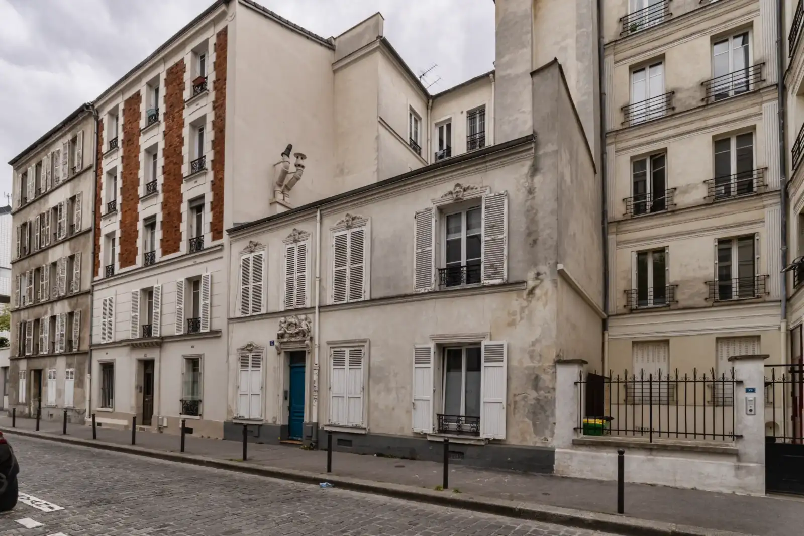 Une ruelle pavée de Paris bordée par de vieux immeubles anciens aux fenêtres persiennes.