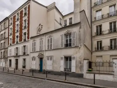 Une ruelle pavée de Paris bordée par de vieux immeubles anciens aux fenêtres persiennes.