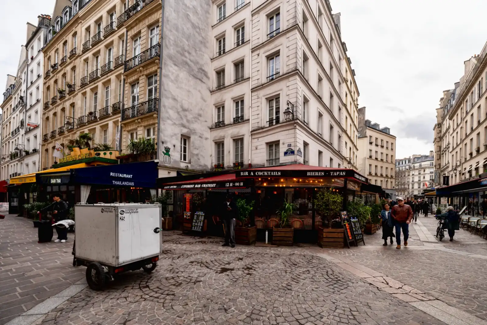 Une rue pavée à Paris avec des immeubles anciens et des terrasses de café.