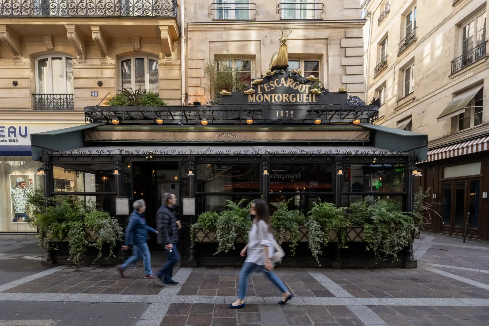 Des passants marchent devant la façade historique du restaurant L'Escargot Montorgueil à Paris.