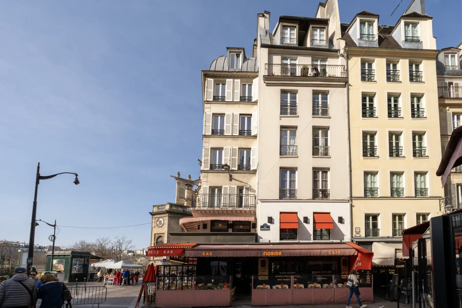 Une vue ensoleillée de la rue Montorgueil avec ses immeubles parisiens et son café.