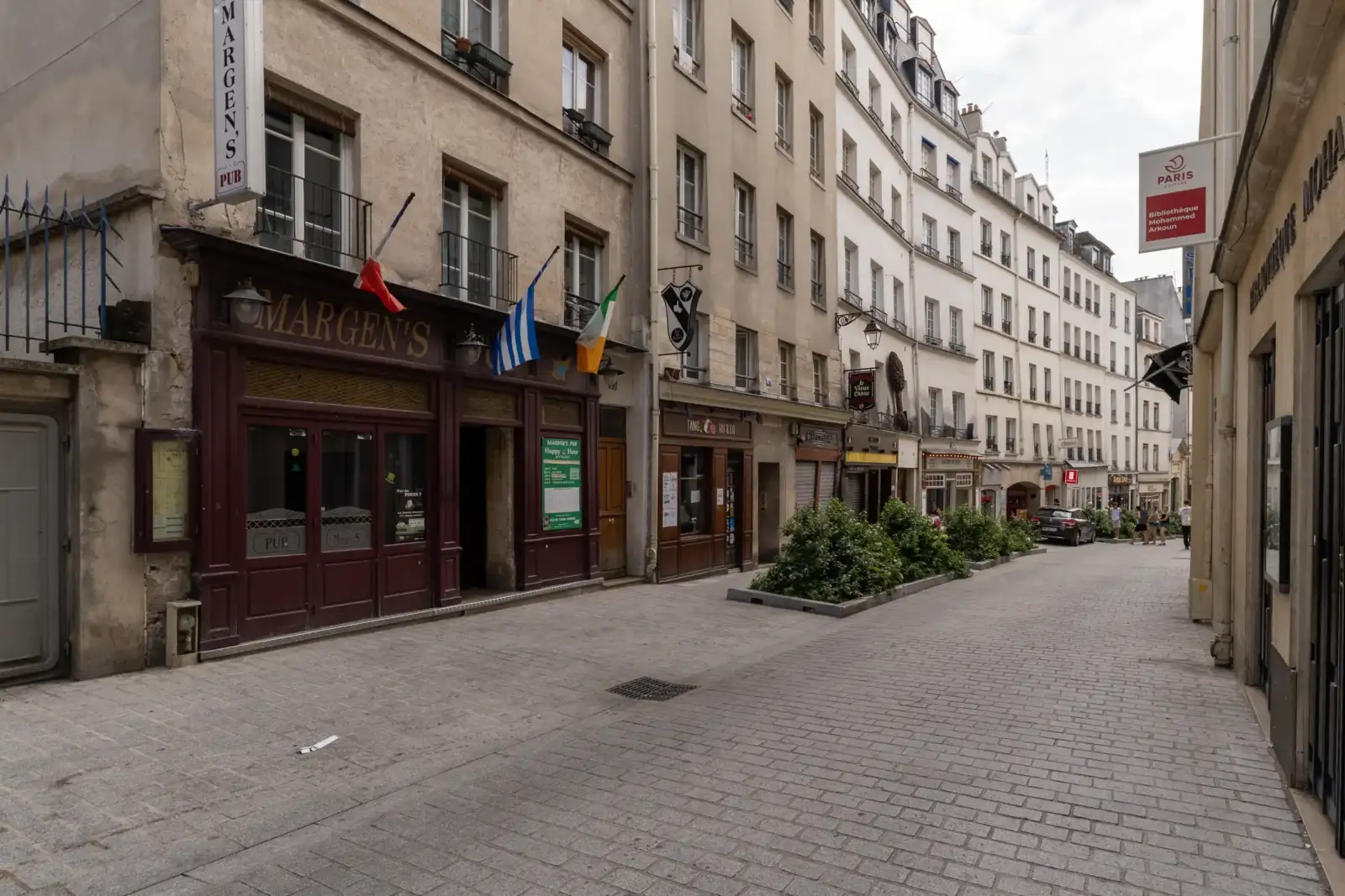 Une rue pavée bordée d'immeubles parisiens anciens avec un pub aux façades sombres.