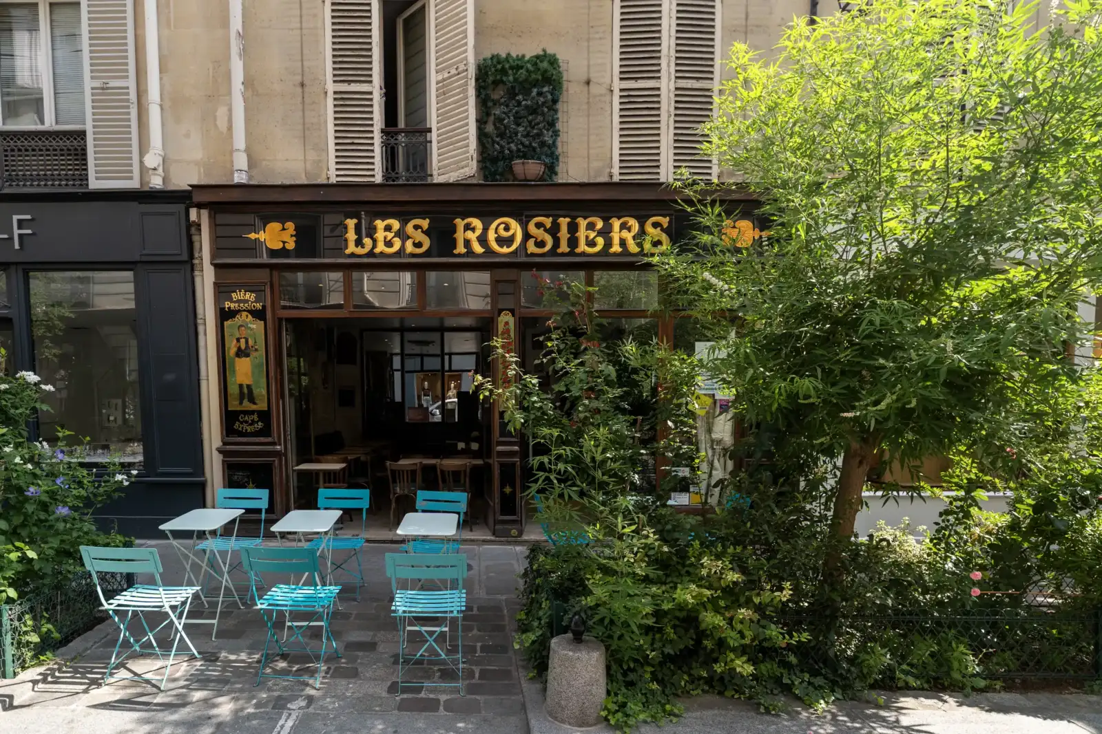 Façade en bois sombre du restaurant Les Rosiers surmontée d un arbre verdoyant.