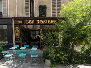 Façade en bois sombre du restaurant Les Rosiers surmontée d un arbre verdoyant.