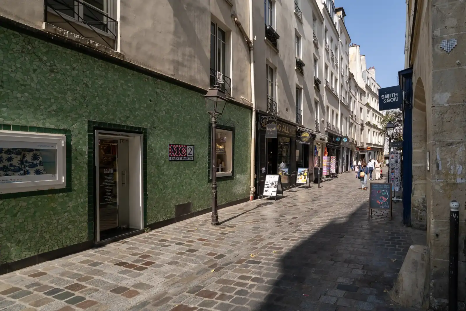 Façade de magasin verte en mosaïque le long d'une rue pavée parisienne.