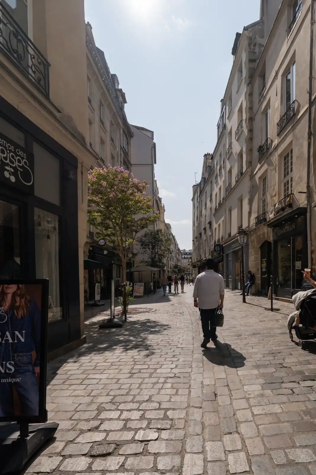 Une vue ensoleillée de la rue des Rosiers pavée avec des piétons.