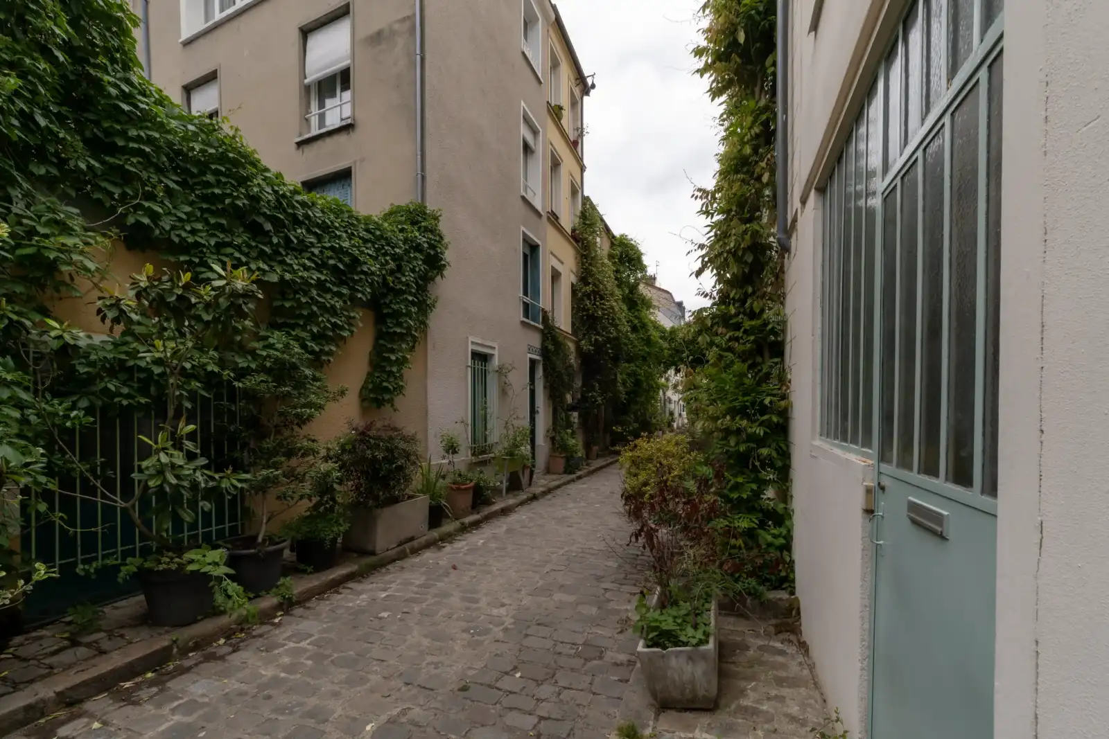 Une ruelle pavée et étroite à Paris, bordée de façades végétalisées.