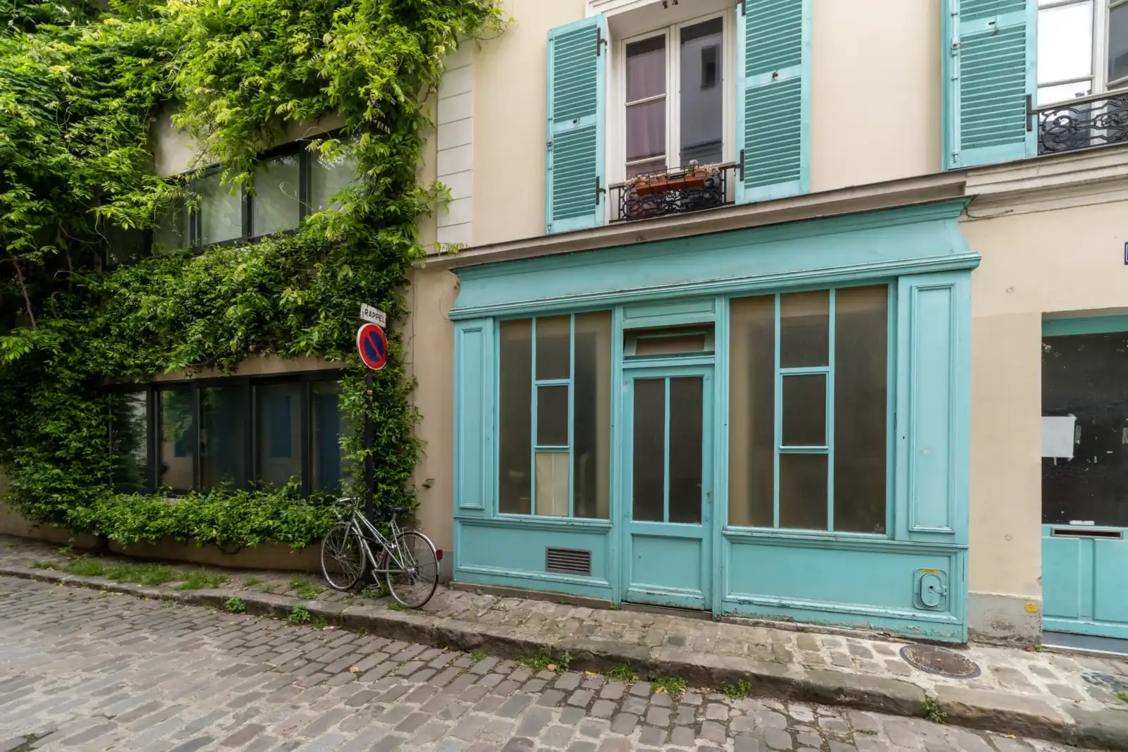 Une façade parisienne pavée met en valeur un élégant magasin bleu turquoise envahi par la verdure.