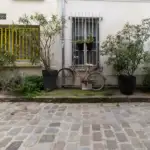 Une bicyclette rouillée est garée contre une façade blanche entourée de plantes en pots.