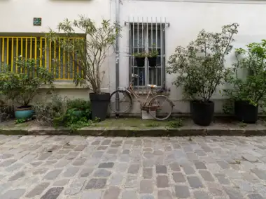 Une bicyclette rouillée est garée contre une façade blanche entourée de plantes en pots.