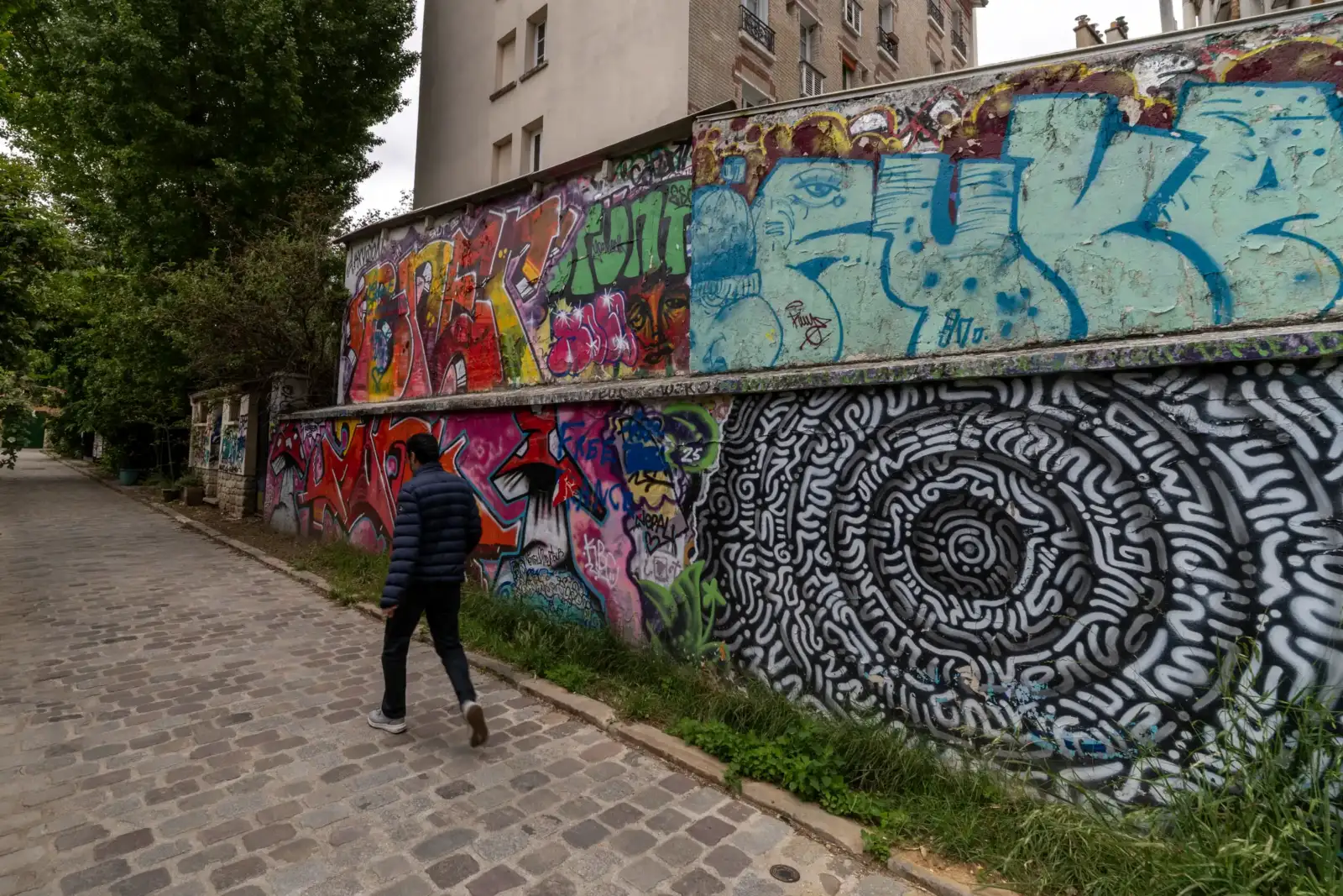 Un homme marche sur un pavé le long d un mur couvert de graffitis colorés.