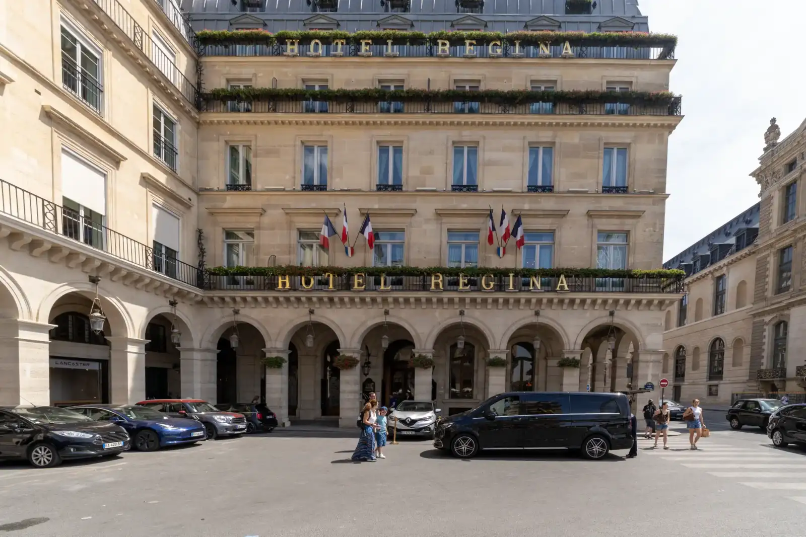 Façade lumineuse et élégante de l'Hôtel Regina, avec des arches et des drapeaux français.