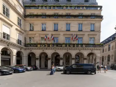 Façade lumineuse et élégante de l'Hôtel Regina, avec des arches et des drapeaux français.