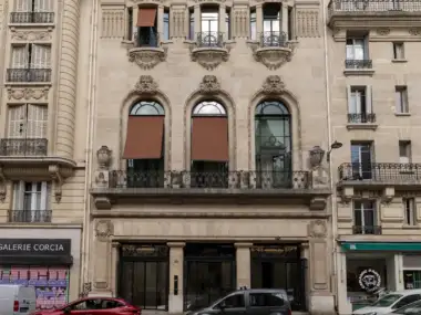 Vue de la façade principale du siège parisien de Jean Paul Gaultier avec des voitures garées.