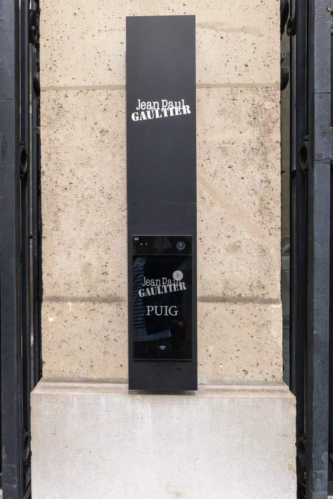 Plaque noire verticale affichant la signalétique Jean Paul Gaultier sur un mur en pierre.