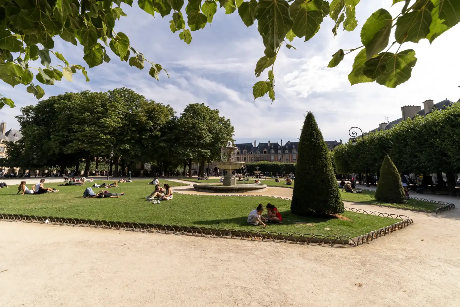 Une fontaine centrale entourée de pelouses verdoyantes et d'arbres sous un ciel ensoleillé.
