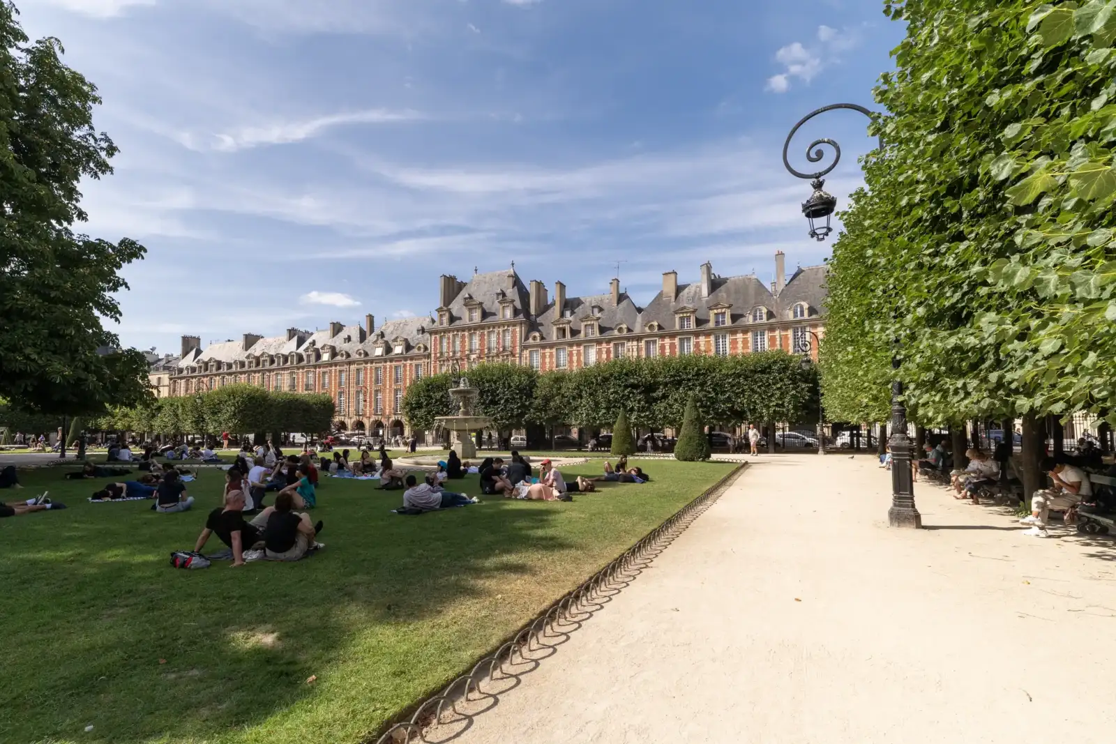 Des personnes profitent d une pelouse ensoleillée devant les façades historiques de la place des Vosges.