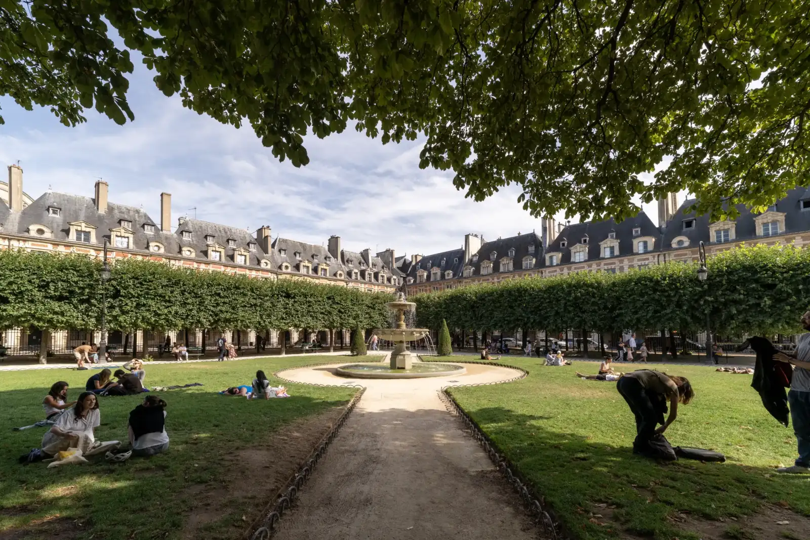 Des personnes se détendent sur la pelouse du Square Louis XIII entouré par les immeubles parisiens.