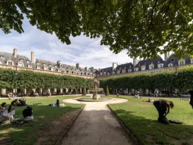 Des personnes se détendent sur la pelouse du Square Louis XIII entouré par les immeubles parisiens.