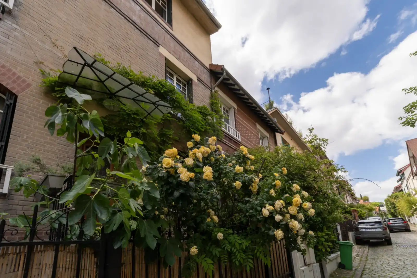 Un immeuble en briques entouré de rosiers jaunes et de verdure dans une rue pavée.