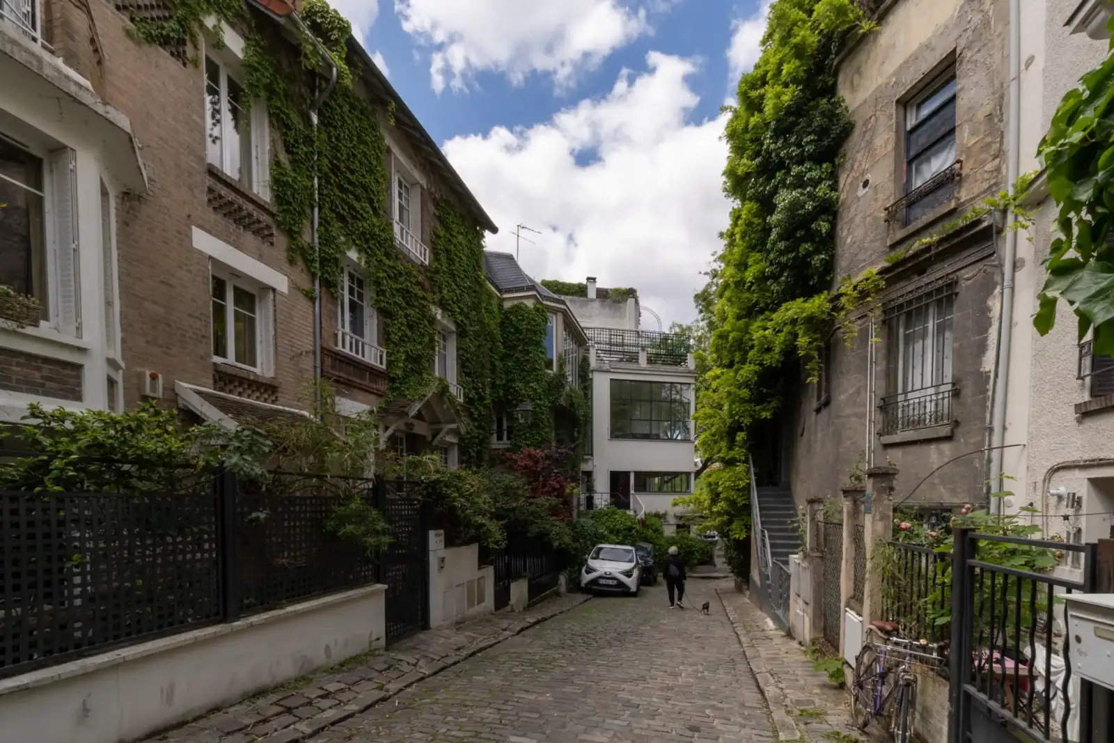 Une allée pavée bordée de maisons verdoyantes sous un ciel partiellement nuageux à Paris.