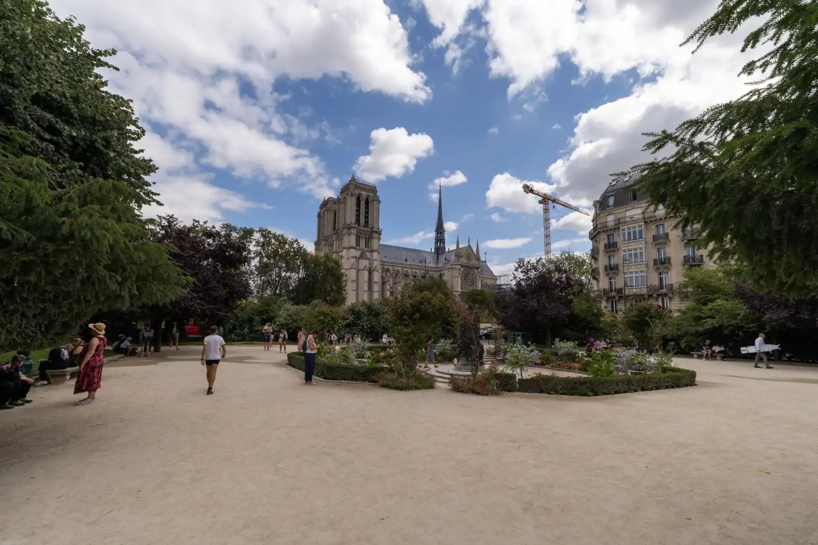 Des promeneurs flânent dans le square René Viviani avec la cathédrale Notre Dame en arrière-plan.