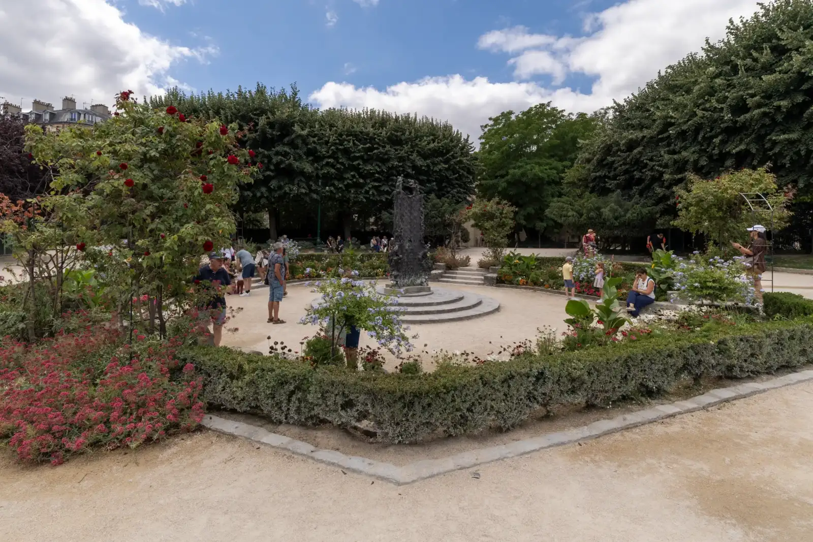 Vue du Square René Viviani à Paris avec des promeneurs et une statue centrale.