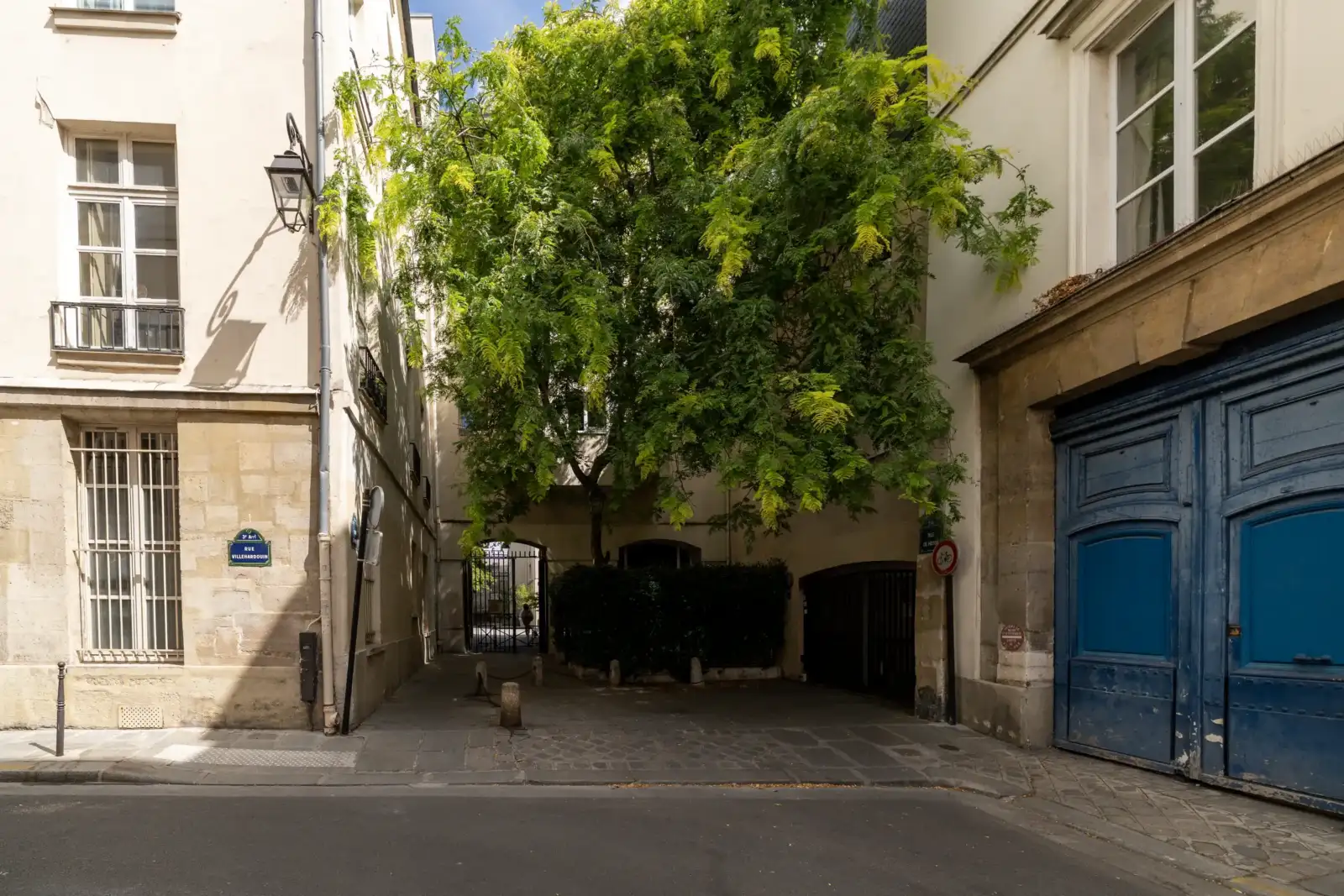 Une belle cour pavée de Paris abrite un arbre verdoyant encadré par des bâtiments.
